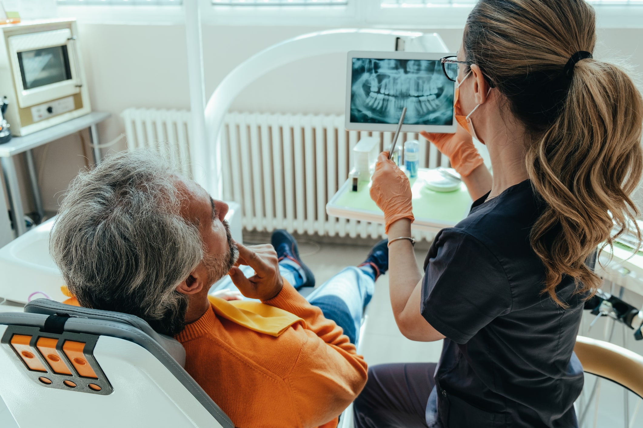 An anonymous woman dentist talking to serious male patient and showing digital tablet with x ray film in dental clinic.